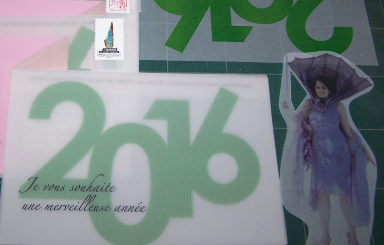 Photo de Faustine Audureau pour le portfolio sur laquelle on voit une enveloppe en calque sur laquelle est indiqué en script : « Je vous souhaite une merveilleuse année » et l’année 2016 dans une autre typo. On voit également une enveloppe similaire déjà fermée et timbrée. Une feuille de calque imprimée mais pas encore pliée. Ainsi que la figure féminine en robe mauve déguisée en Fée des Lilas imprimée sur du calque.