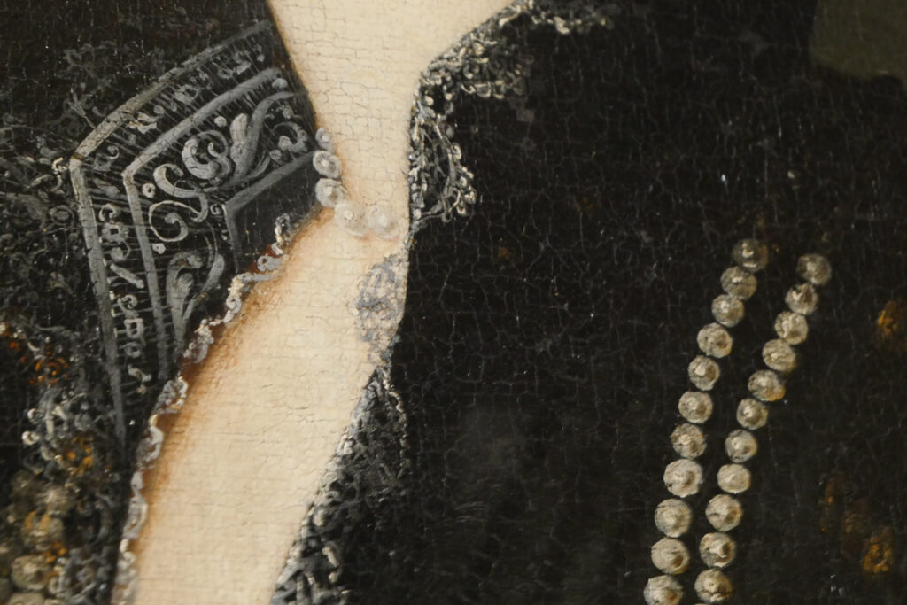 Photographie pour le portfolio d'un détail d'un tableau d'Artemisia Gentileschi sur lequel on voit le col noir d'une veste, ainsi que le corsage en dentelle en dessous, ainsi qu'un collier.